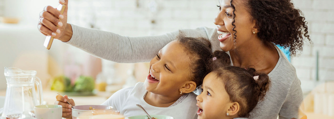 Smiling mother and two daughters taking a selfie at breakfast.
